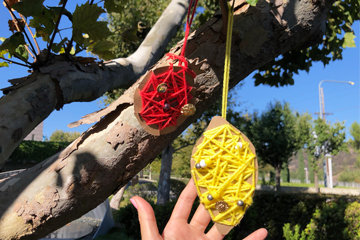 Two fruit cutouts with yarn strung around them hanging from a tree outdoors