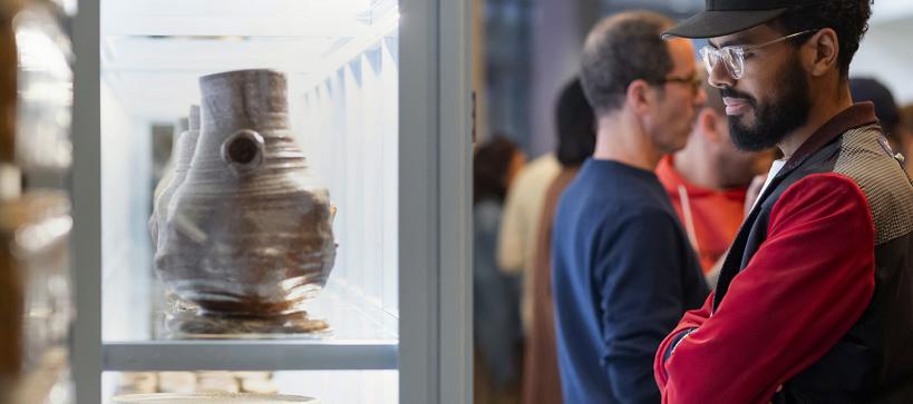 A man looks at pottery in a gallery case.