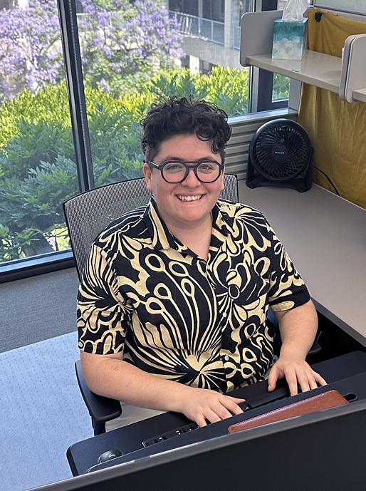 A person sitting at a desk looking up and smiling while typing at a computer.