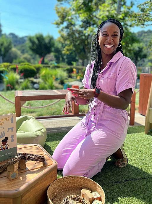 A woman sits outside with a table full of books and games, smiling.