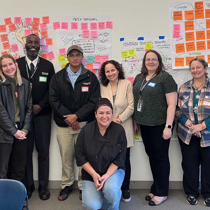 Seven adults standing in front of post it boards smiling.