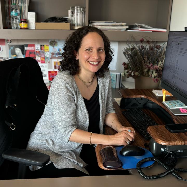 A woman sitting in an office at her desk smiling.