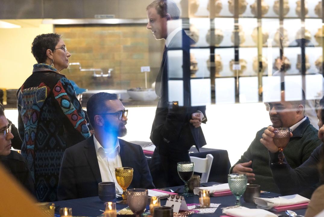 Through a window, people can be seen sitting around a table with a display case reflected above them