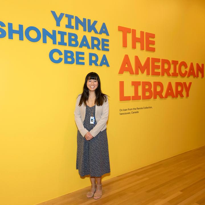 A woman smiles for a picture in front of a museum wall that reads "the American Library"