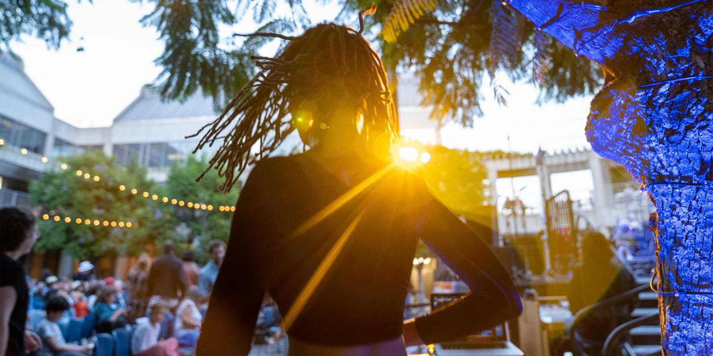 Seen from behind, a DJ operates a turntable to a crowd of people sitting in chairs before an outdoor concert in the Skirball's courtyard.