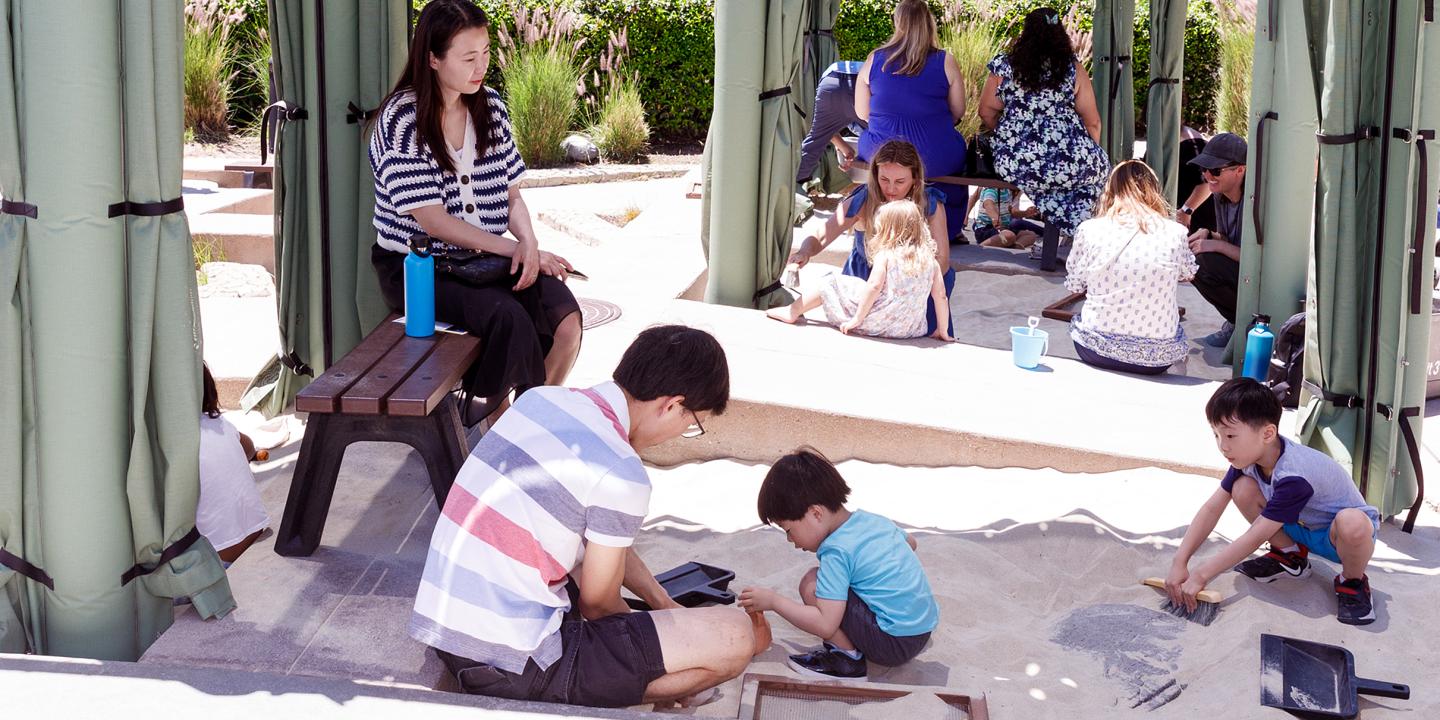 A family with kids digging through a sand box uncovering replica artifacts