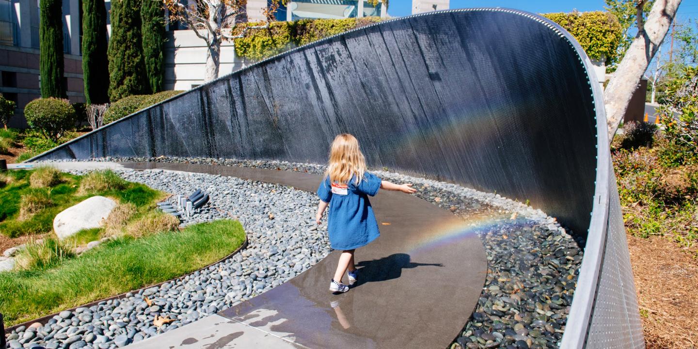 A young girl running through an arbor mist that creates a rainbow.