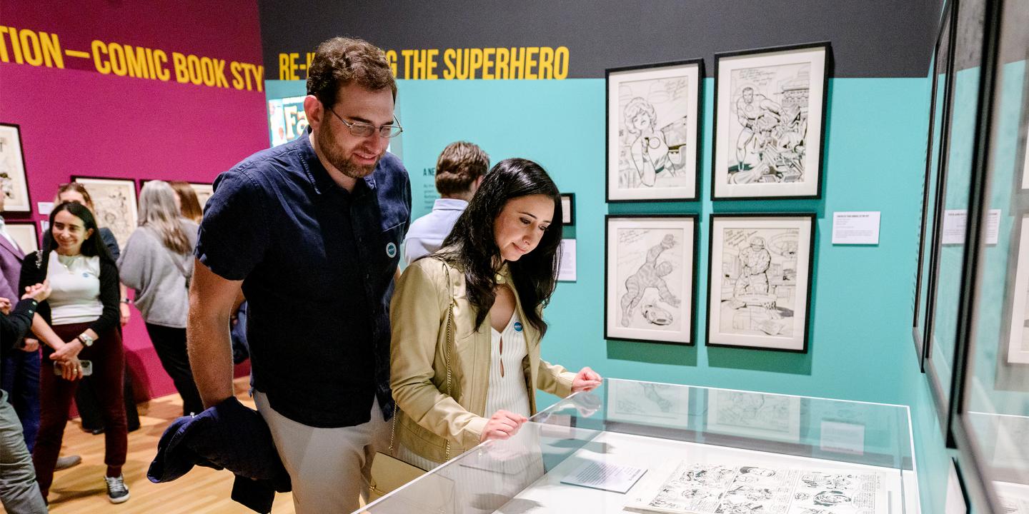 A man and a woman in a gallery look at a case with comic book art in it.