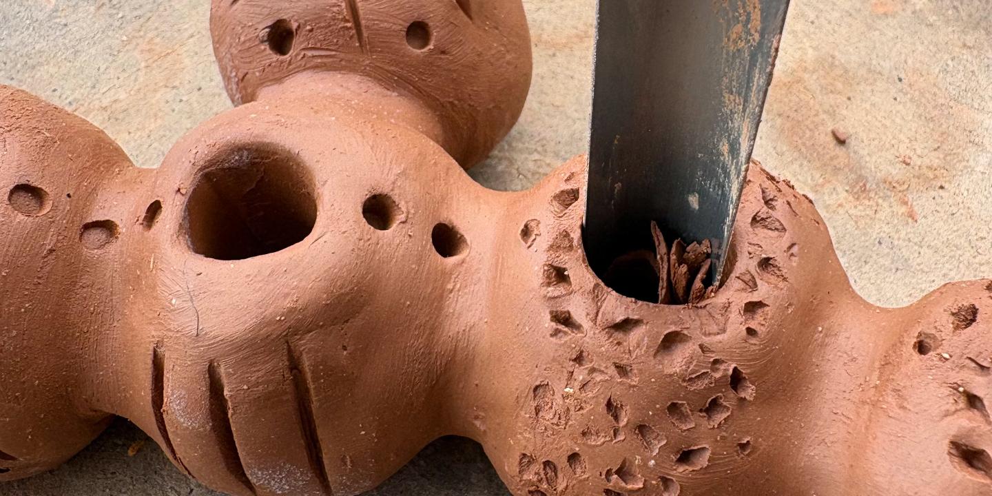 A ceramic sculpture in clay being worked on with a tool.
