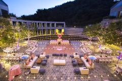 A couple dancing in an outdoor courtyard with a lily pond decorated with lights, tables, lounge areas and a dance floor that has the name Natalie projected on it. .