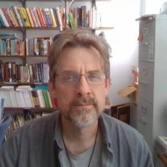 Charles Hatfield sits in an office facing the camera with a full bookshelf behind him.