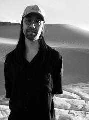 A black and white phot of a man posing for a picture in a desert landscape.