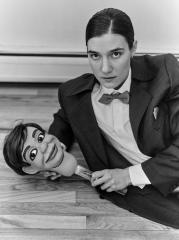 A black and white image of a woman in a suit holding a puppet head.
