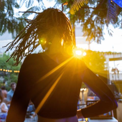 Seen from behind, a DJ operates a turntable to a crowd of people sitting in chairs before an outdoor concert in the Skirball's courtyard.