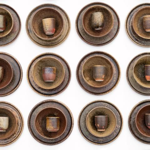 A set of plates, bowls, and cups made from pottery set up in a row.