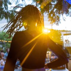 Seen from behind, a DJ operates a turntable to a crowd of people sitting in chairs before an outdoor concert in the Skirball's courtyard.