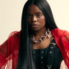The artist Vagabon, dressed in red and black, looking directly into the camera.