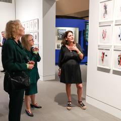 An artist stands in front of their collages and talks about them to guests