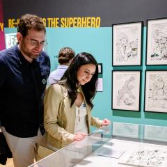 A man and a woman in a gallery look at a case with comic book art in it.