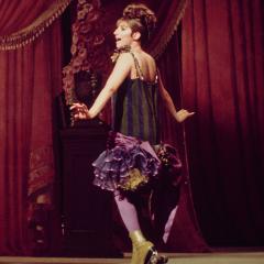 A woman sings on stage in a fancy short dress and roller-skates